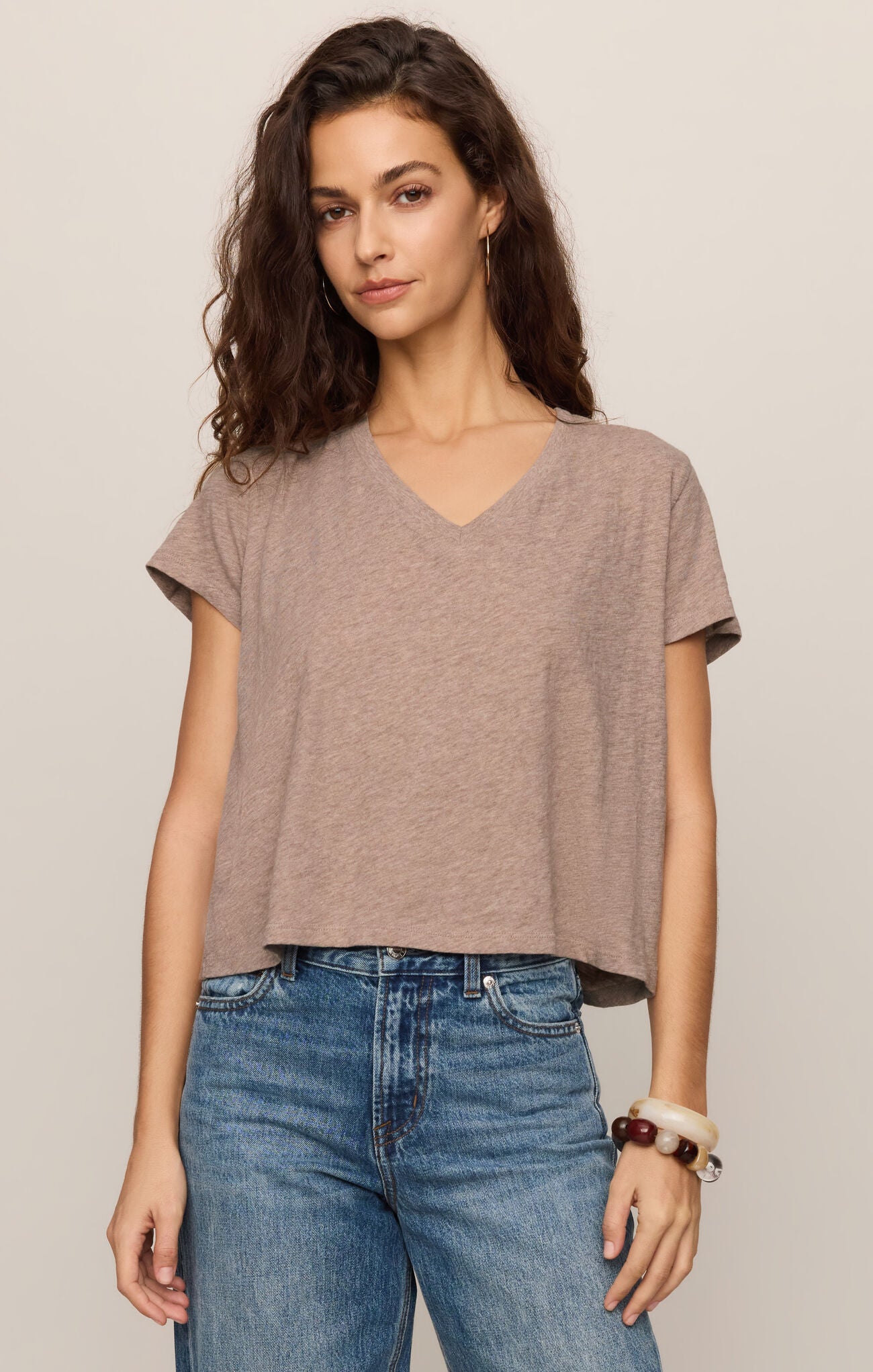 Woman wearing a brown t-shirt and blue jeans against a beige background