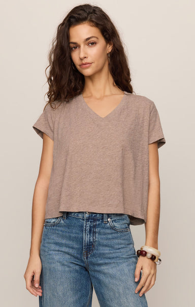 Woman wearing a brown t-shirt and blue jeans against a beige background