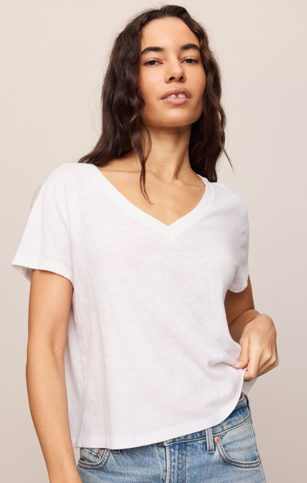 Woman wearing a plain white t-shirt and blue jeans against a beige background