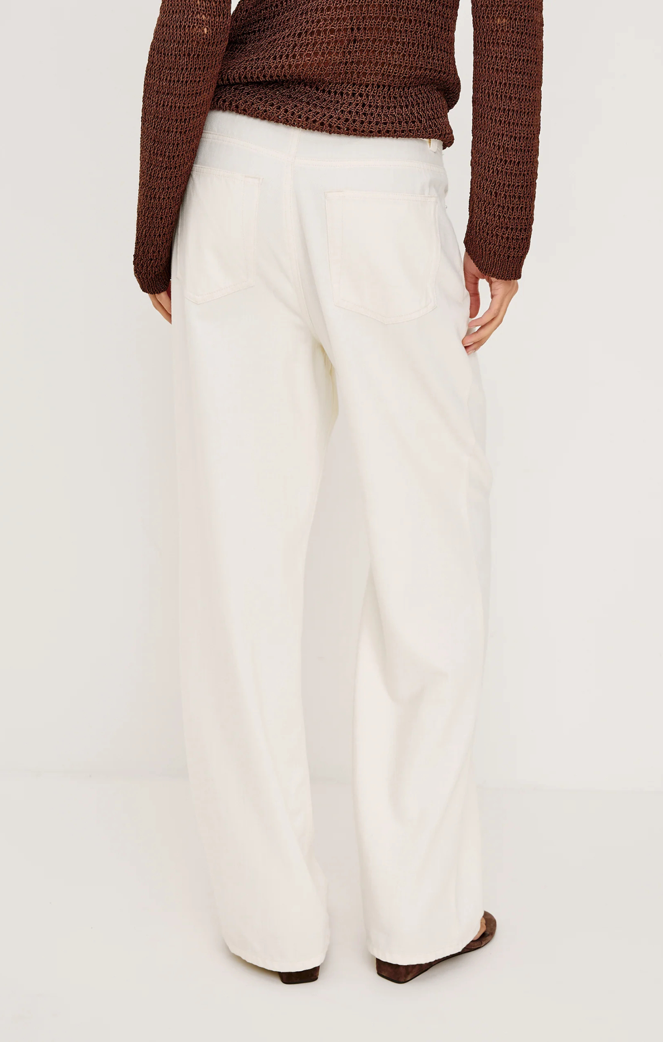 Person wearing white pants and a brown sweater on a plain background