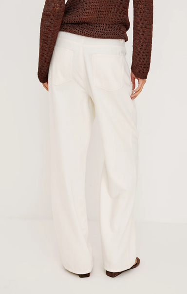 Person wearing white pants and a brown sweater on a plain background