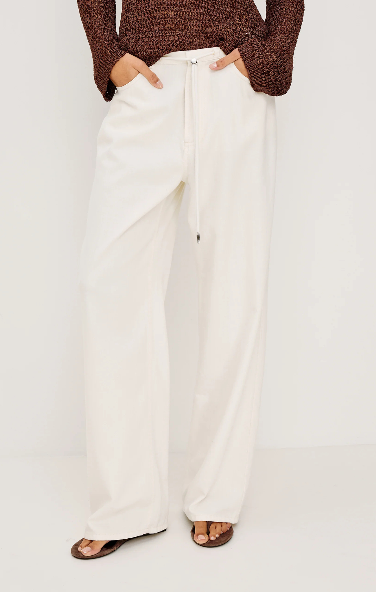 Person wearing white pants and a brown top on a plain background