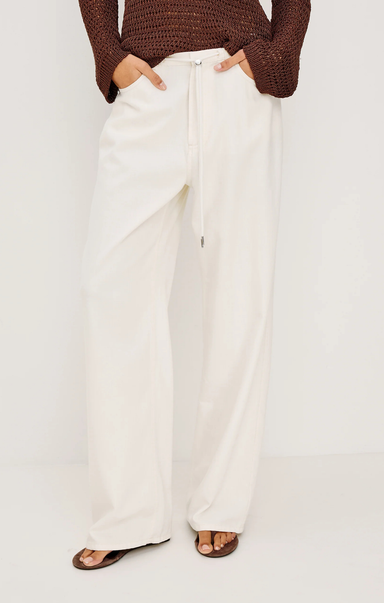 Person wearing white pants and a brown top on a plain background