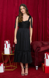 Woman in a black dress standing in front of a red curtain with gift boxes and a couch.
