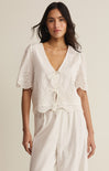 Woman wearing a white lace top and pants against a beige background