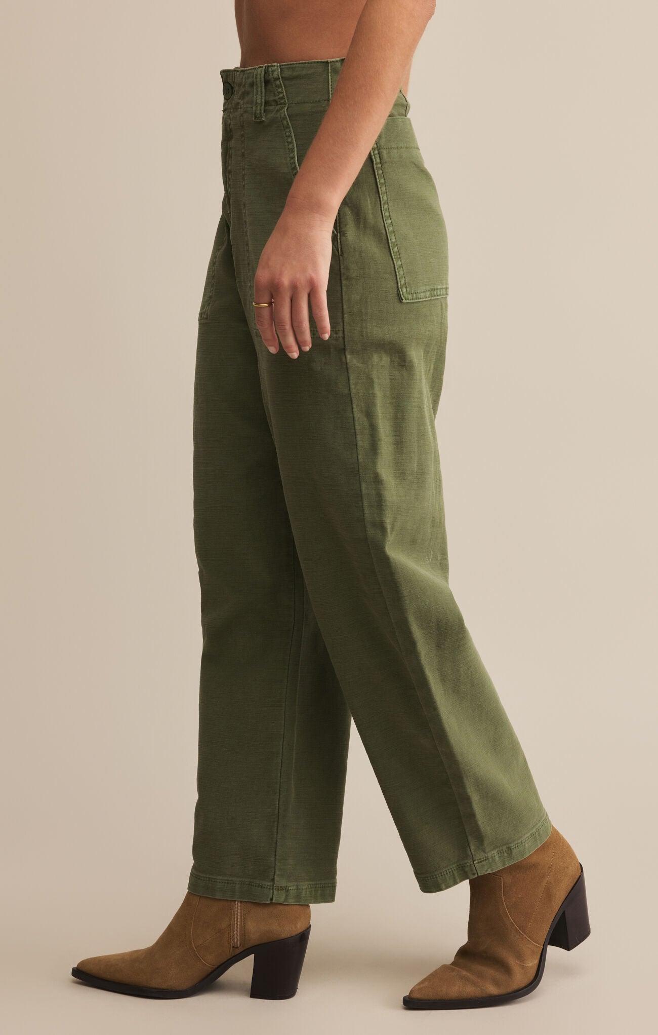 A person standing wearing olive twill pants and brown boots.