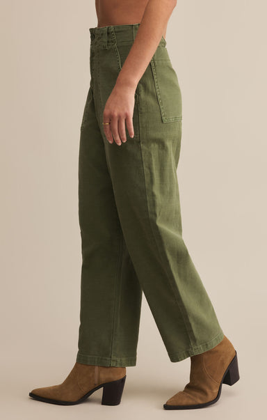 A person standing wearing olive twill pants and brown boots.