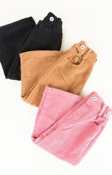 Three pairs of folded corduroy pants in black, brown, and pink on a white background.
