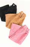 Three pairs of folded corduroy pants in black, brown, and pink on a white background.