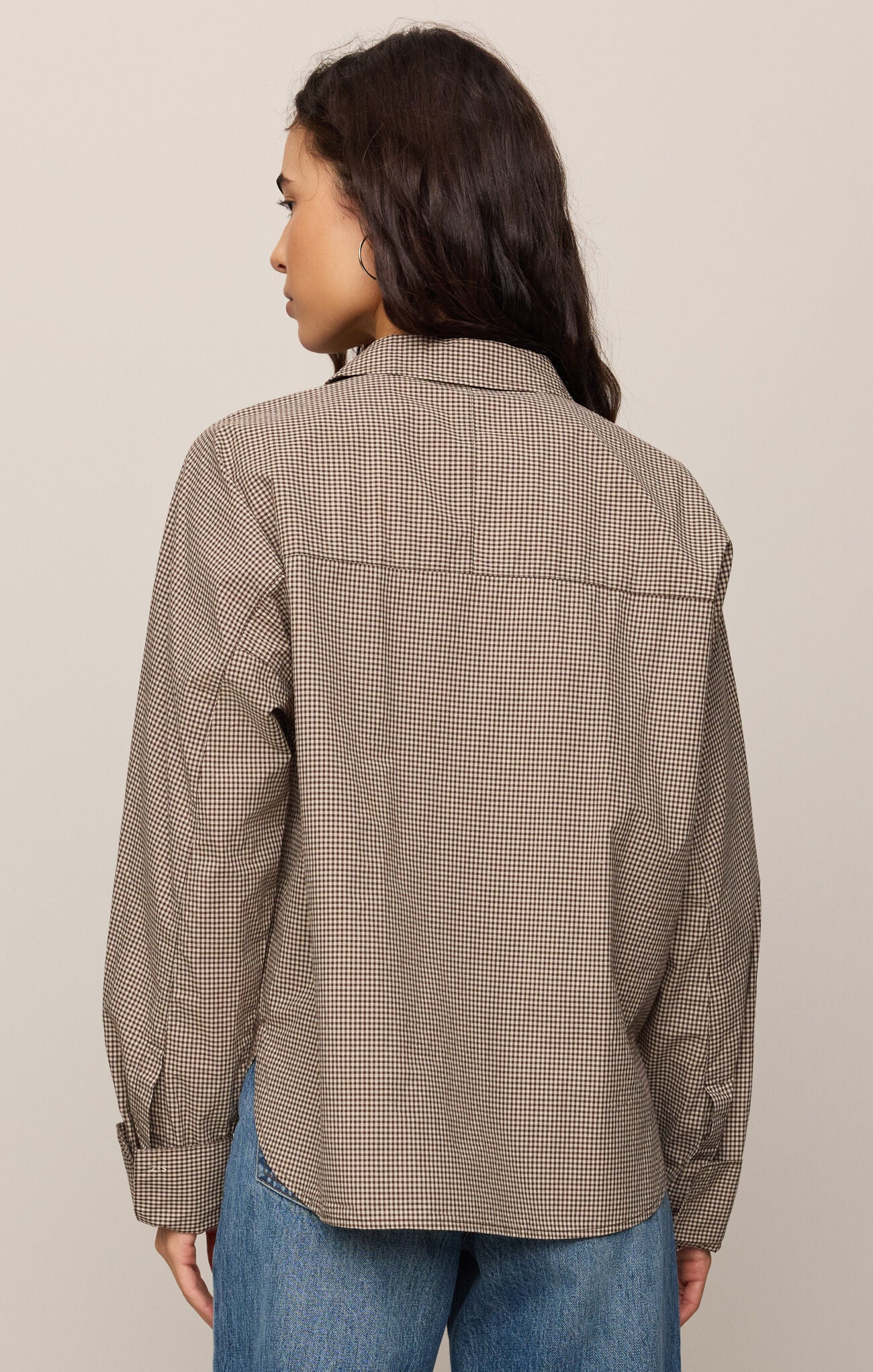 Woman wearing a brown checkered shirt and blue jeans on a beige background