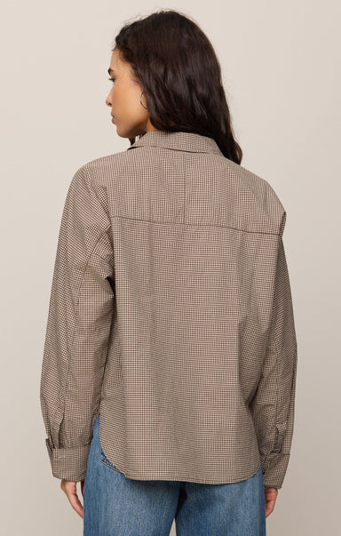 Woman wearing a brown checkered shirt and blue jeans on a beige background