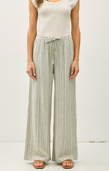 Woman wearing light-colored striped pants and a white top on a plain background