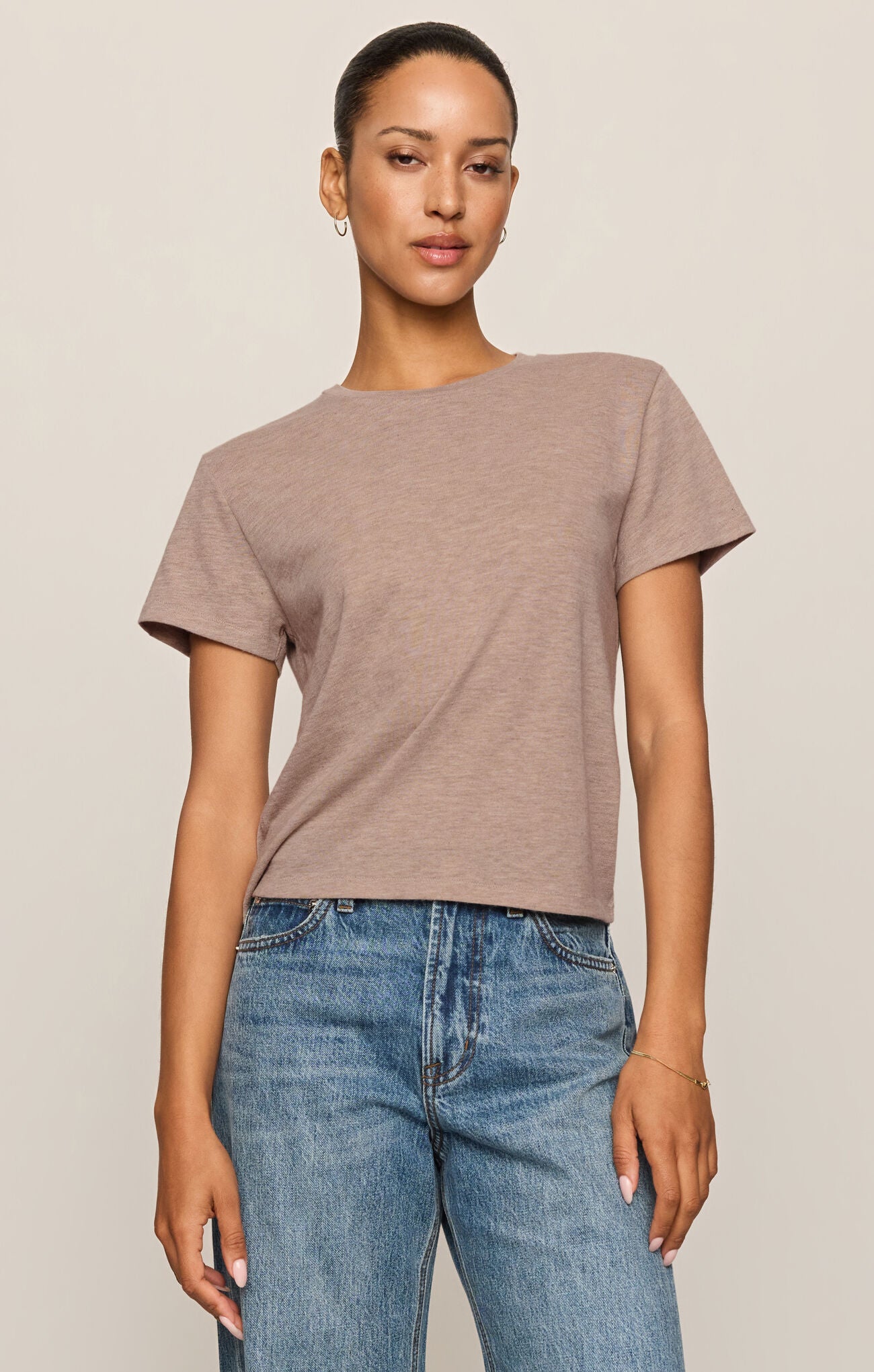 Woman wearing a brown t-shirt and blue jeans against a beige background