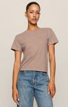 Woman wearing a brown t-shirt and blue jeans against a beige background
