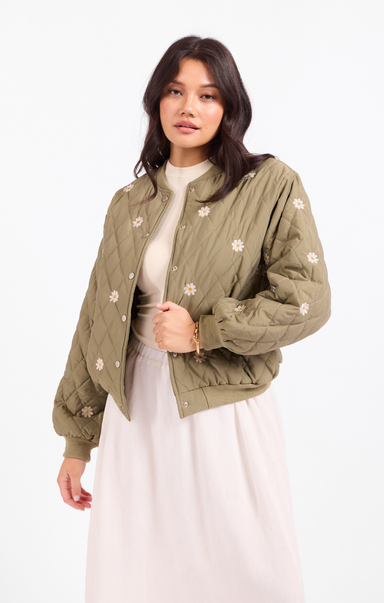 Woman wearing a green quilted jacket with floral patterns on a white background