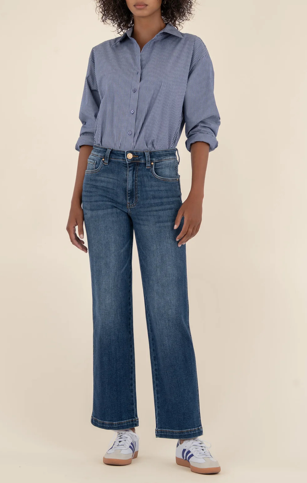 Person wearing a blue button-up shirt and jeans on a beige background