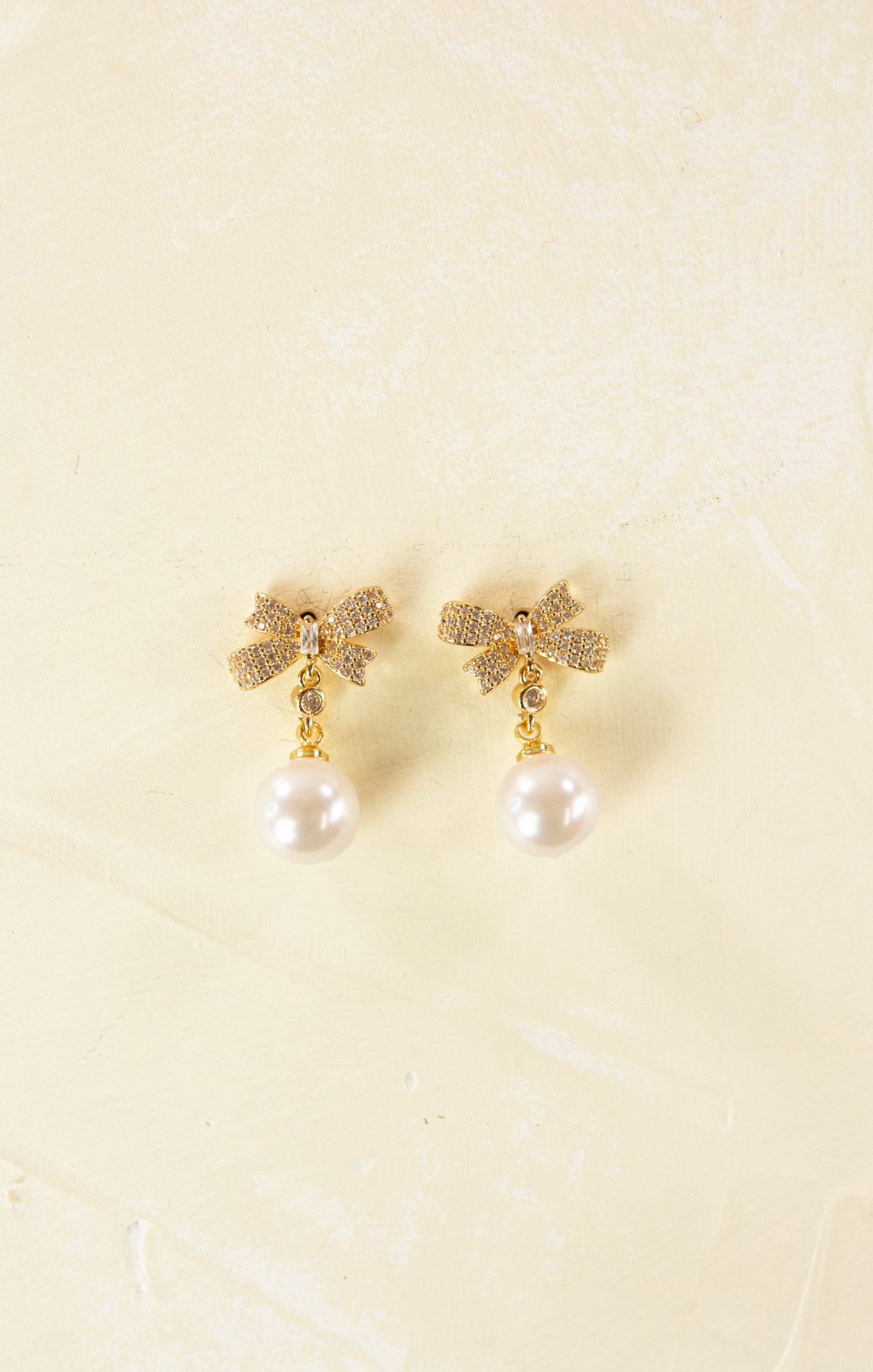 Gold earrings with pearl drops on a beige background
