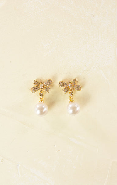 Gold earrings with pearl drops on a beige background