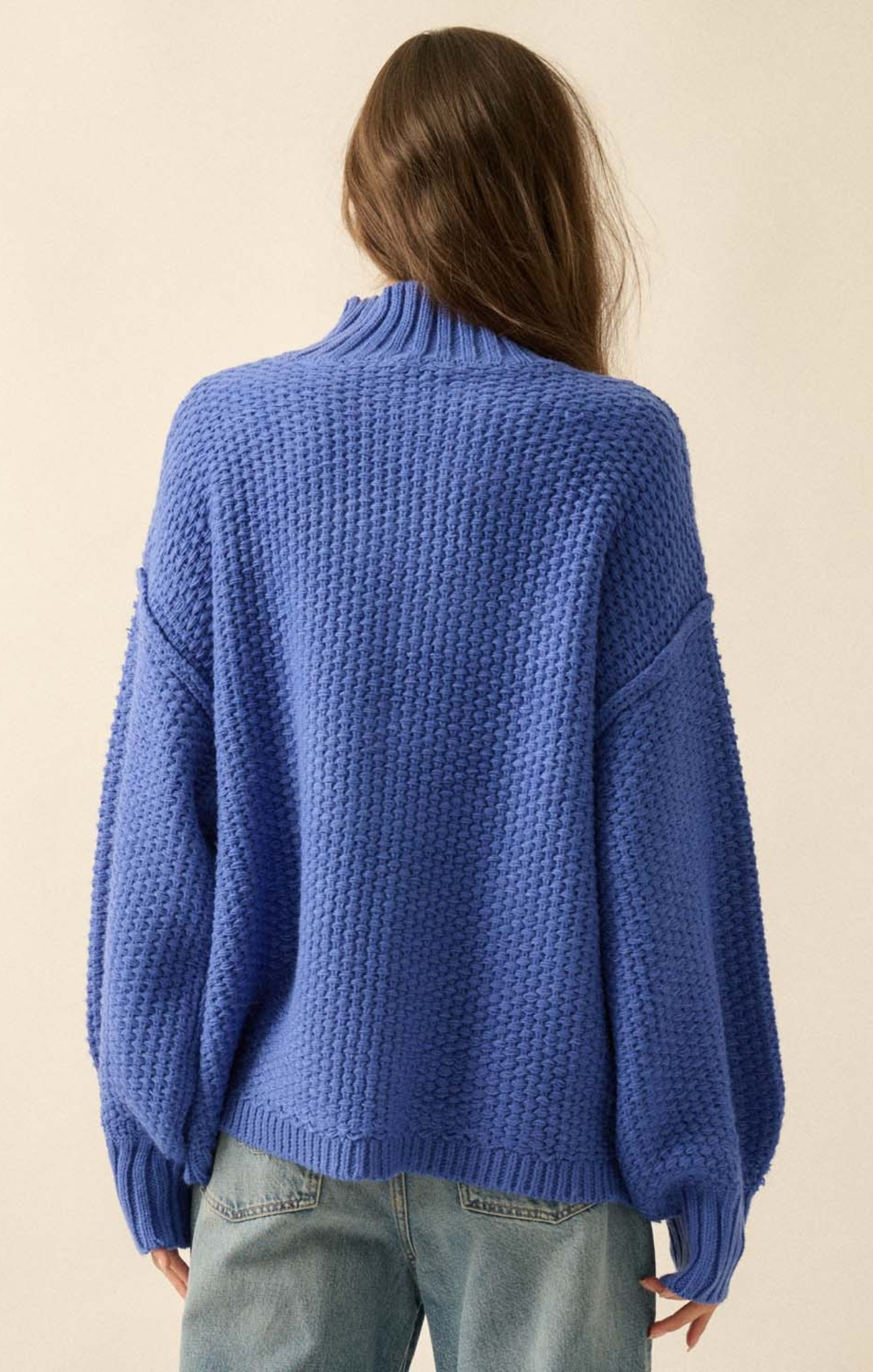 Person wearing a blue knitted sweater against a beige background