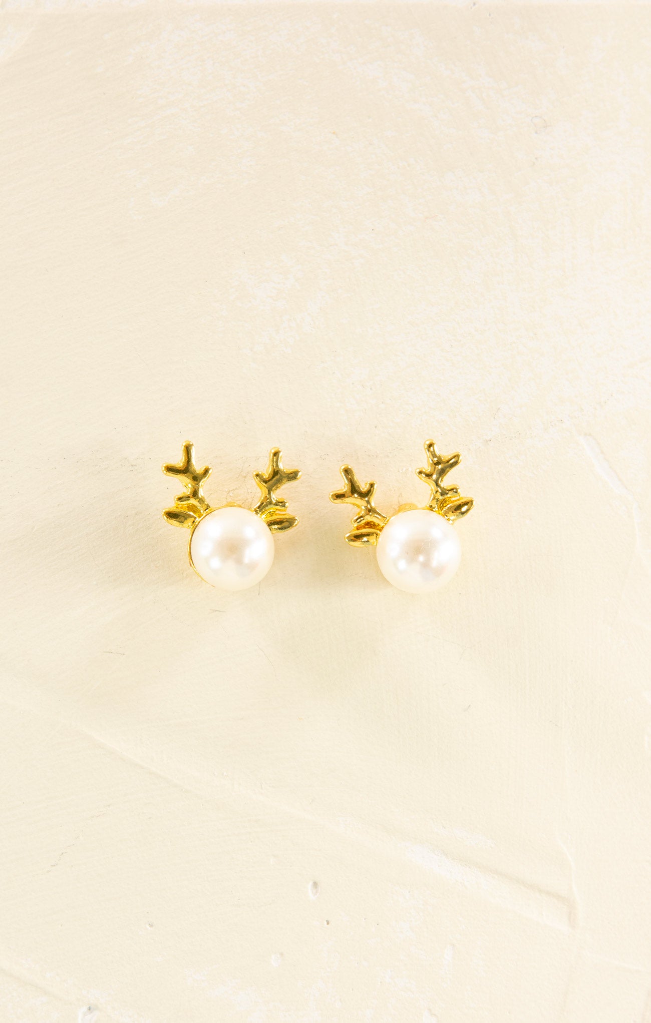 Pair of gold antler earrings with pearl centers on a beige background