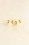 Pair of gold antler earrings with pearl centers on a beige background