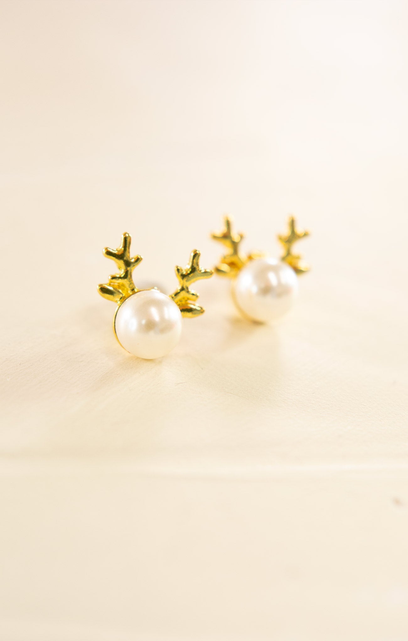Pair of pearl earrings with gold antler-like designs on a beige background