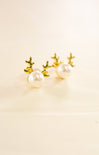 Pair of pearl earrings with gold antler-like designs on a beige background