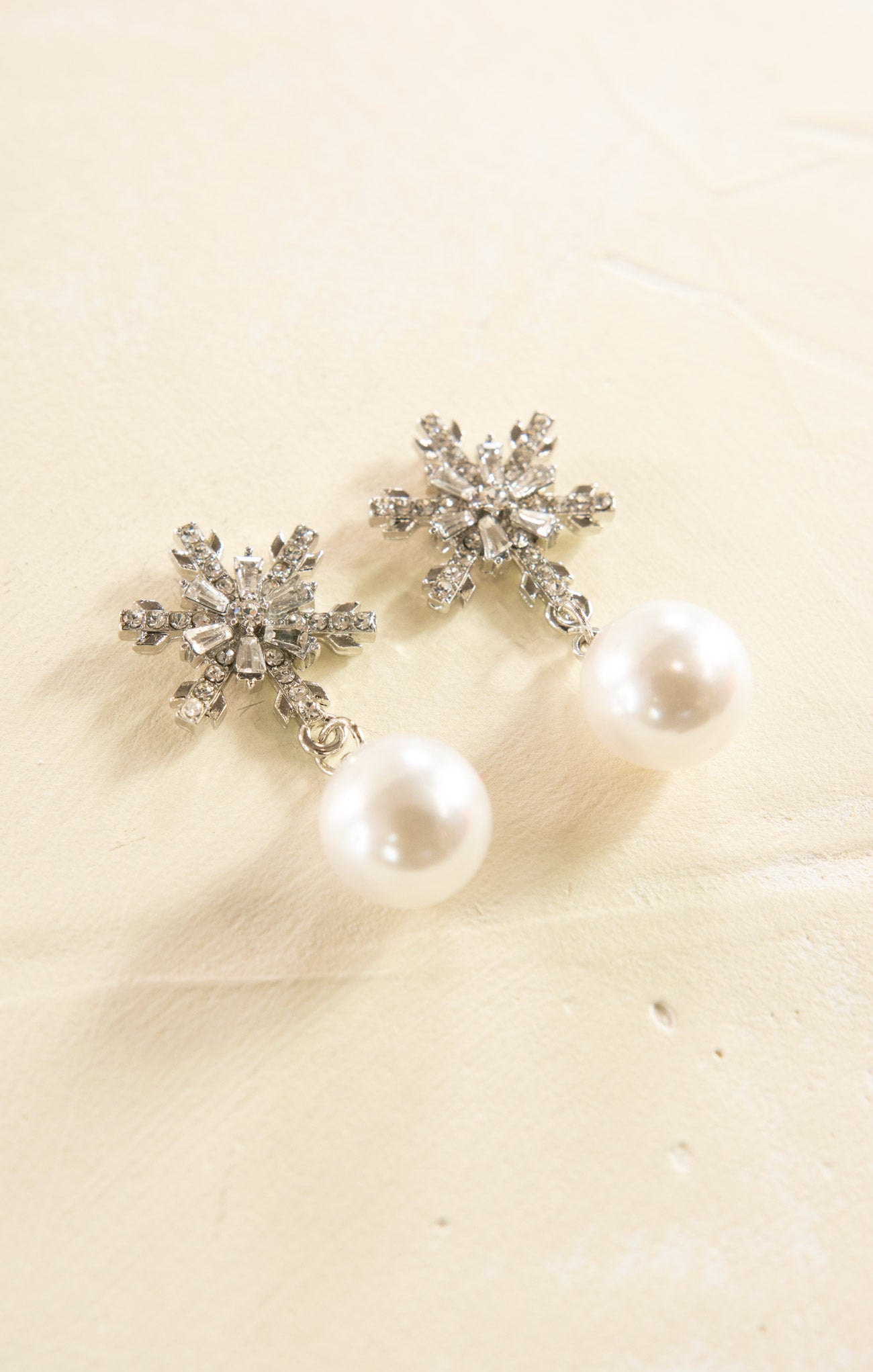 Snowflake-shaped earrings with pearl-like stones on a beige background