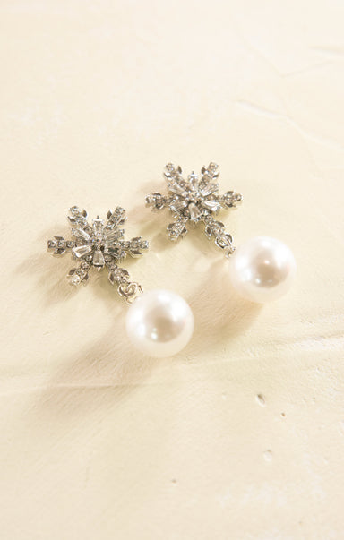 Snowflake-shaped earrings with pearl-like stones on a beige background