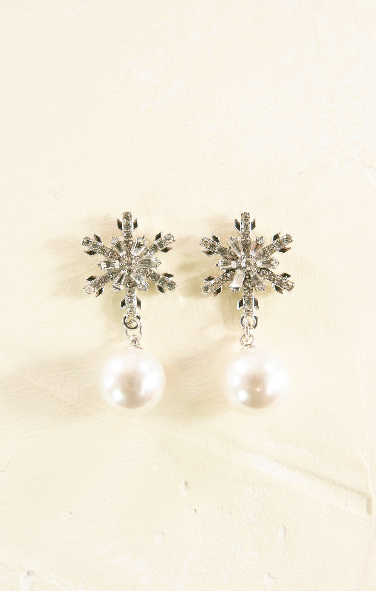 Pair of snowflake earrings with pearl drops on a beige background