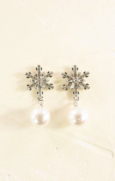 Pair of snowflake earrings with pearl drops on a beige background