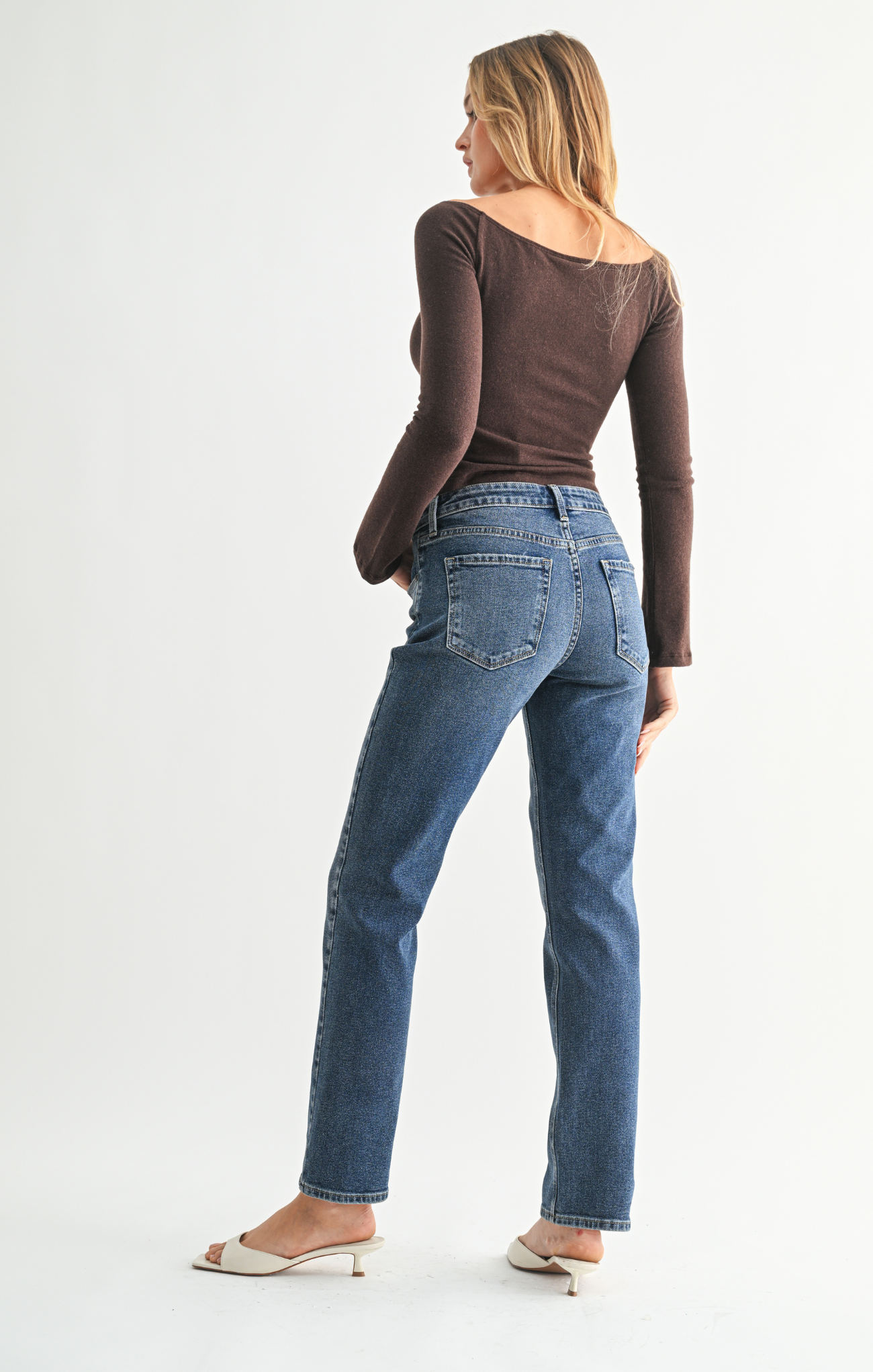 Woman wearing blue jeans and a brown top on a white background