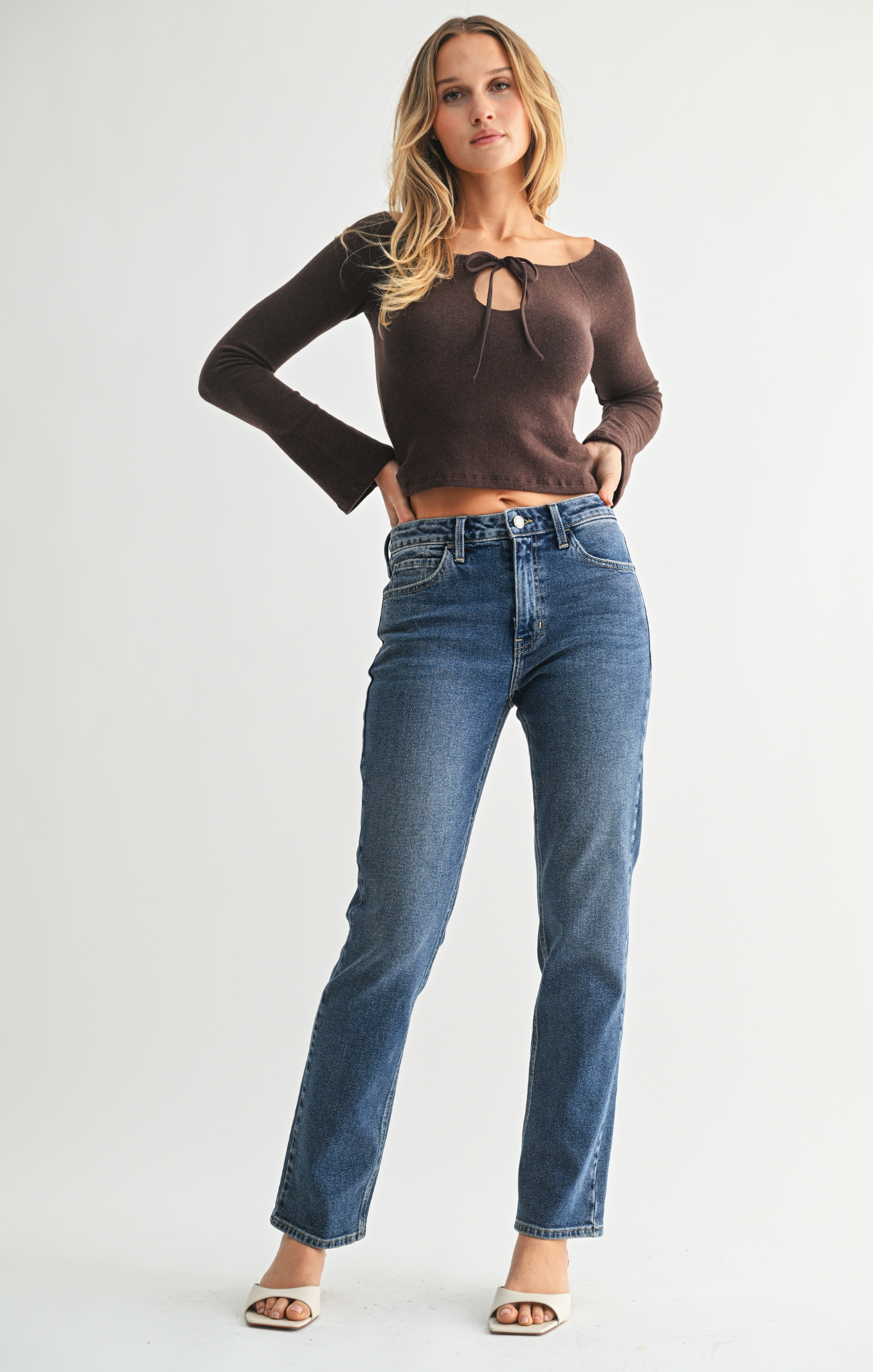 Woman wearing a brown long-sleeve top and blue jeans on a white background