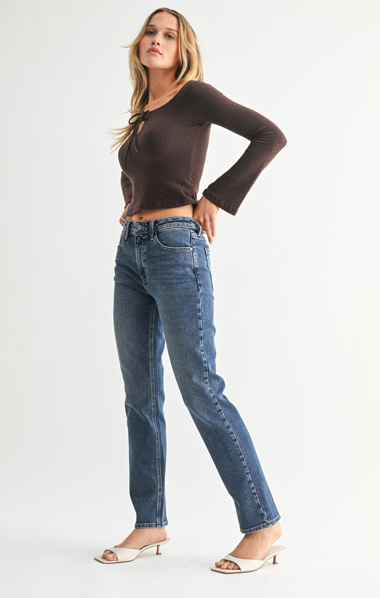 Woman wearing blue jeans and a brown top on a white background