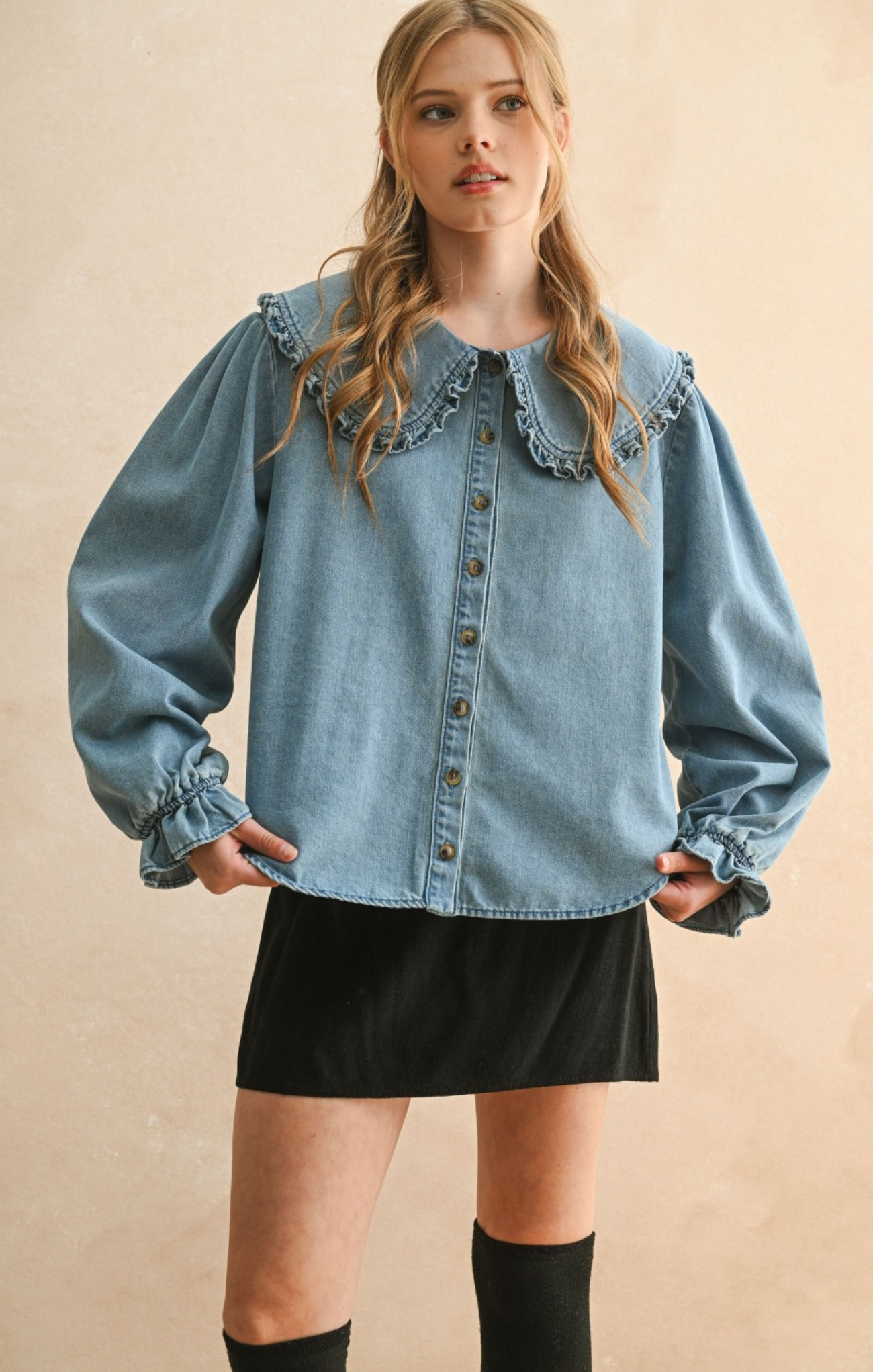 Woman wearing a denim blouse with ruffled collar and long sleeves on a beige background