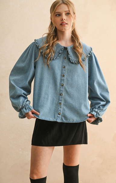 Woman wearing a denim blouse with ruffled collar and long sleeves on a beige background