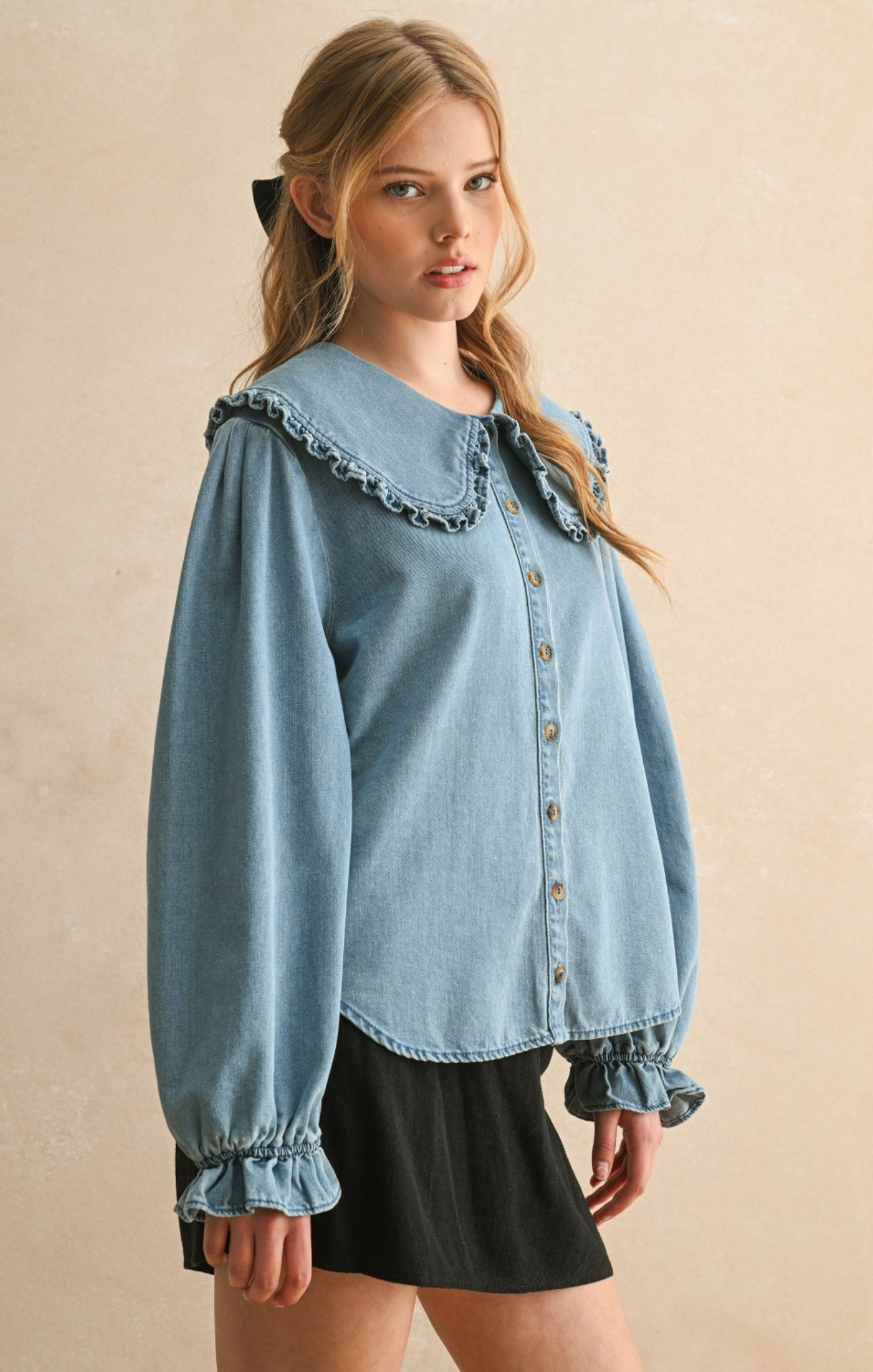 Woman wearing a light blue denim blouse with ruffled collar against a beige background