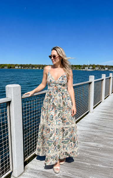 Woman in a floral dress standing on a dock by a body of water.