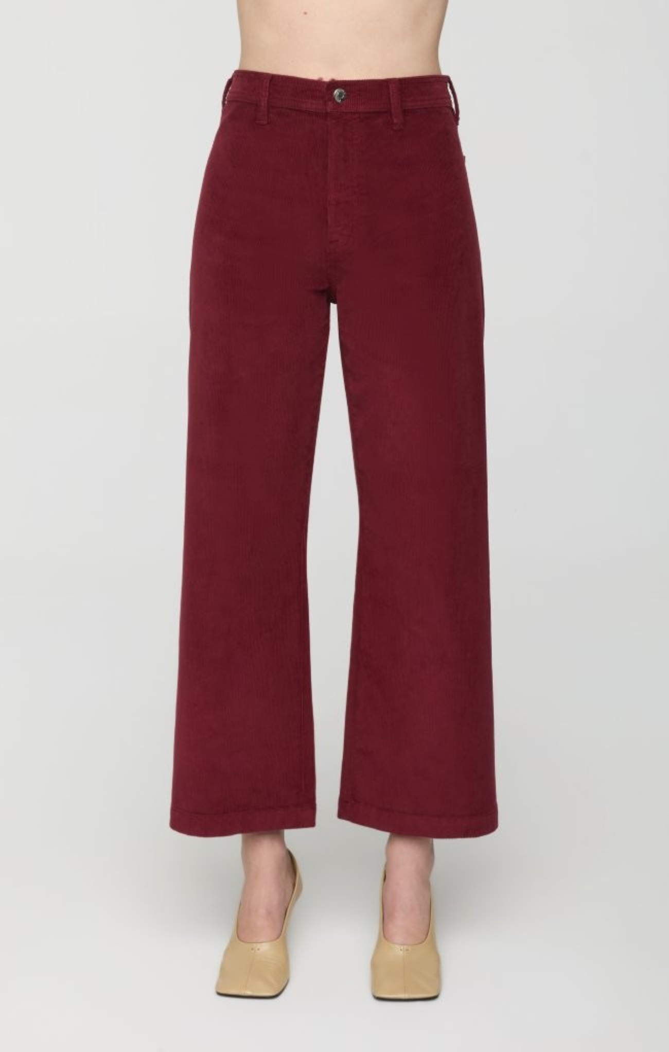 A person wearing high-waisted, wide-leg cropped pants in a deep burgundy corduroy fabric, paired with beige heels, shown against a plain light gray studio background.