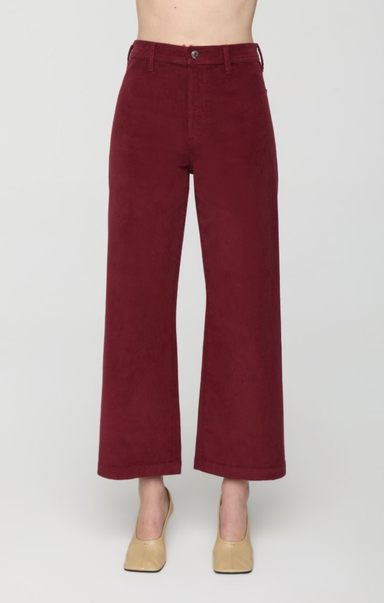 A person wearing high-waisted, wide-leg cropped pants in a deep burgundy corduroy fabric, paired with beige heels, shown against a plain light gray studio background.