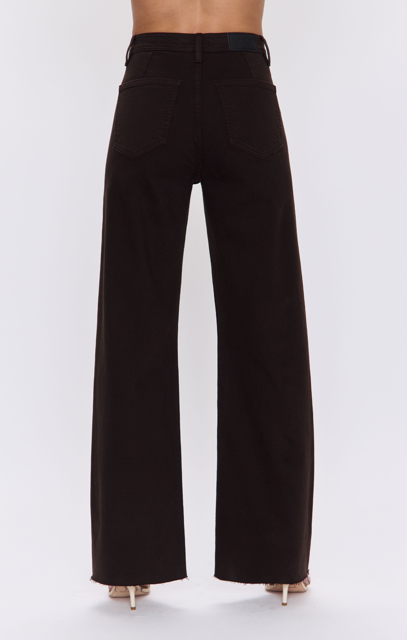 Black wide-leg jeans shown from the back on a model, featuring a high waist and straight, relaxed leg, paired with beige high-heeled sandals against a light gray background.