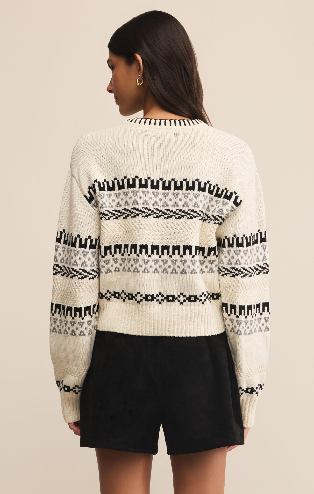 Person wearing a white sweater with black pattern on a beige background
