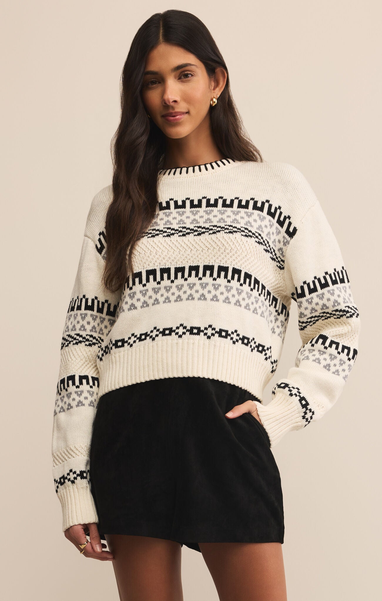 A woman wearing a white and black geometric patterned sweater with long sleeves, paired with a black skirt.