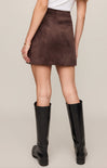 Person wearing a brown suede skirt and black knee-high boots on a beige background