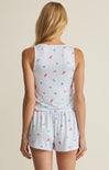 Woman wearing a light blue sleeveless top and shorts with colorful patterns on a beige background