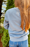 Person wearing a light blue sweatshirt with a white floral design on the back, standing outdoors.