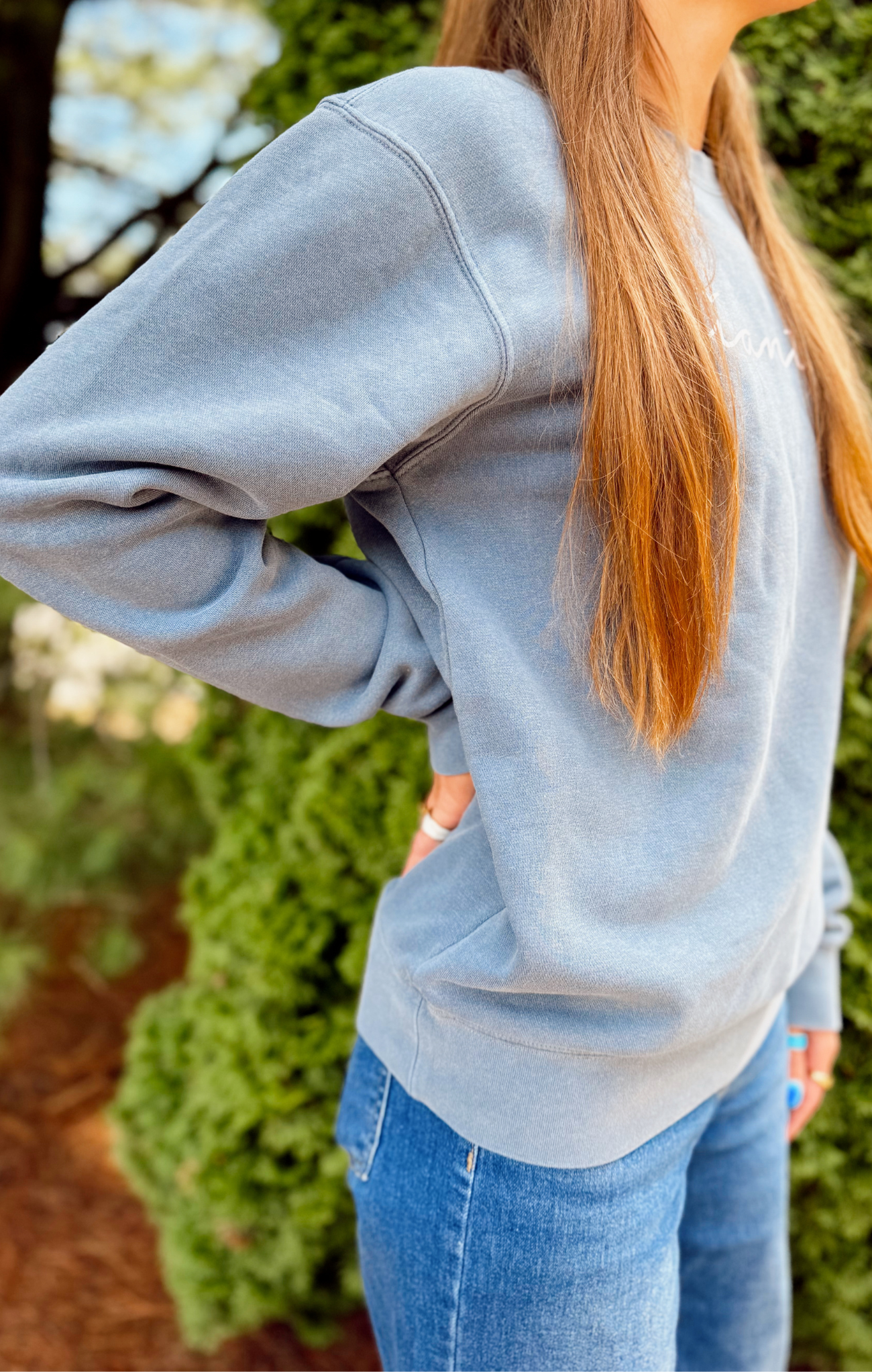 Person wearing a light gray sweatshirt and blue jeans with a blurred green background