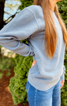 Person wearing a light gray sweatshirt and blue jeans with a blurred green background