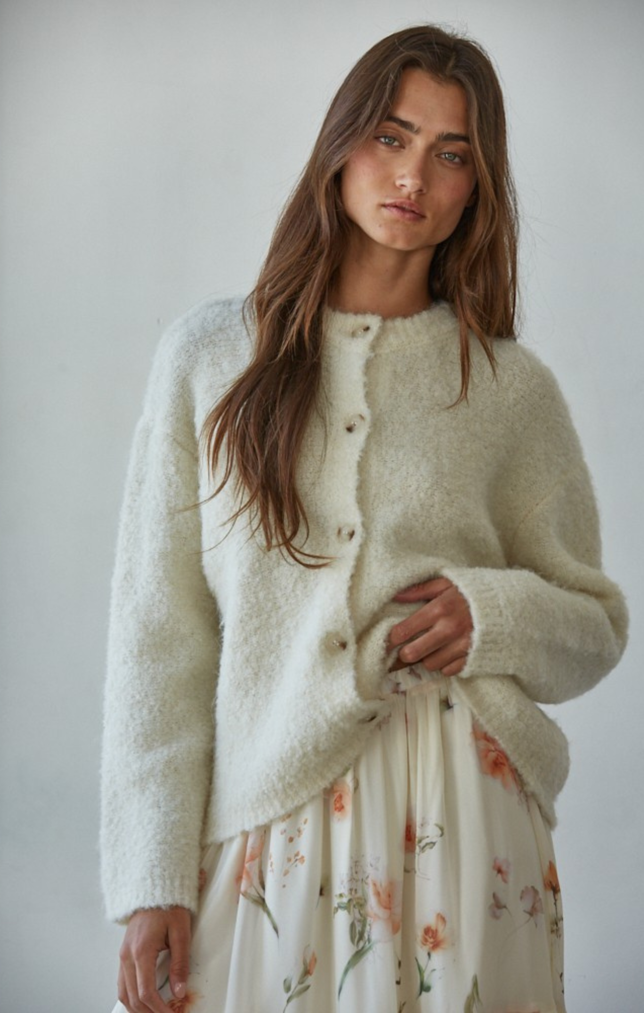 Woman wearing a cream cardigan over a floral dress against a plain background