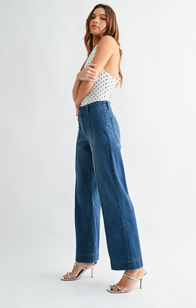 Woman wearing a polka dot top and blue wide-leg jeans on a white background